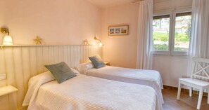 Ein Schlafzimmer mit zwei Betten, einem Sessel, einem Fenster und einer Wandleuchte.