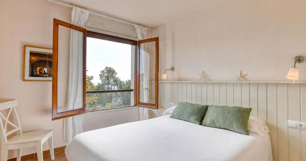 Una camera da letto con un letto, una sedia, una finestra con tende e un punto luce a parete.