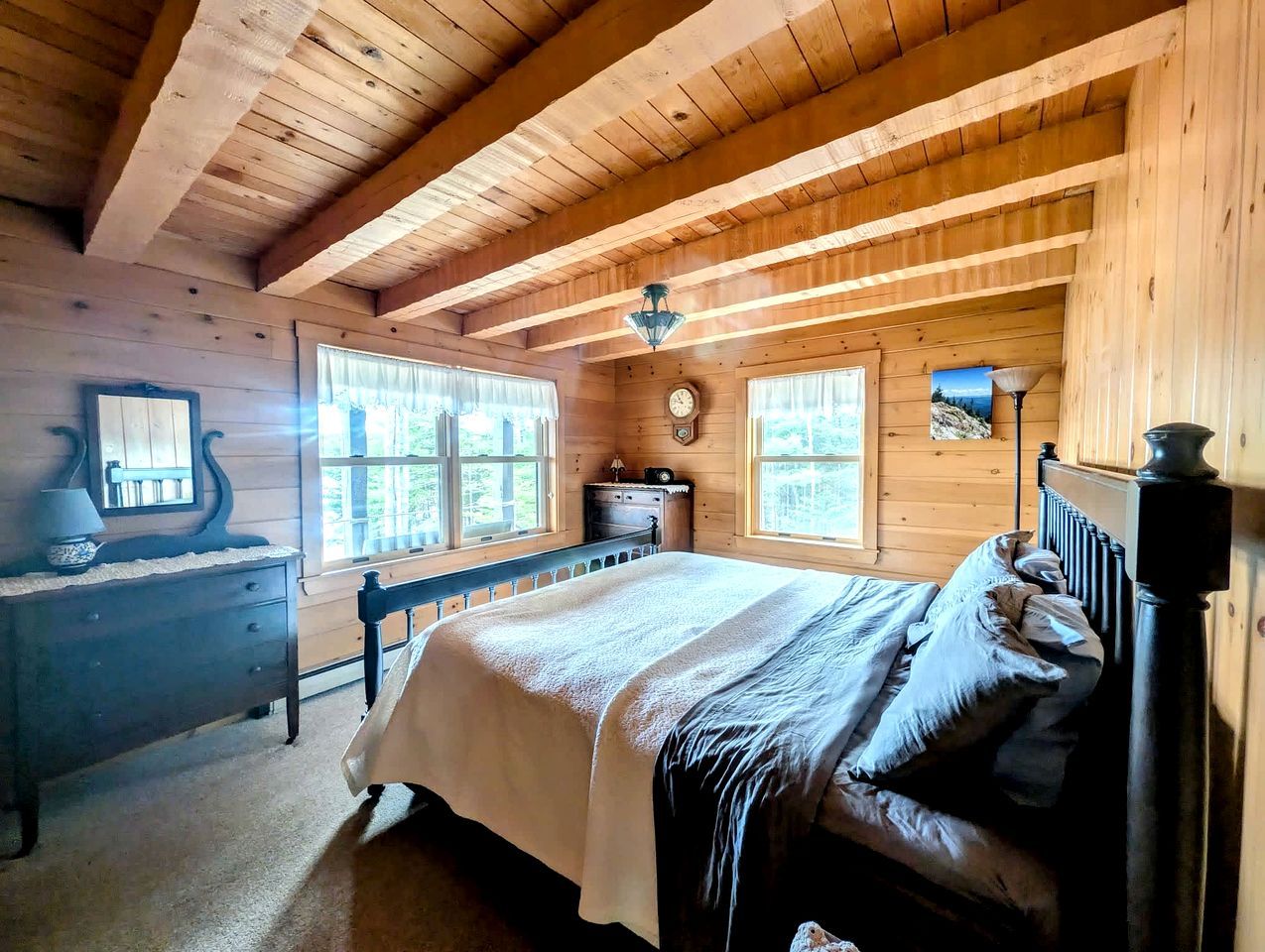 A wooden cabin bedroom with a bed, dresser, and a clock on the wall.