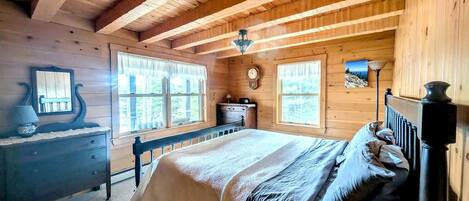 A wooden cabin bedroom with a bed, dresser, and a clock on the wall.