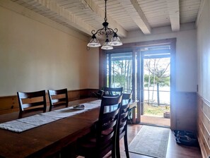 A dining area with a wooden table, chairs, a woven placemat, and a hanging light fixture. - Waterfront Cabin Retreat with Deck Swing in Lamoine Point, Maine (Lamoine Point)
