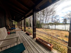 A wooden deck with outdoor seating and planters, overlooking a river and forested area. - Waterfront Cabin Retreat with Deck Swing in Lamoine Point, Maine (Lamoine Point)