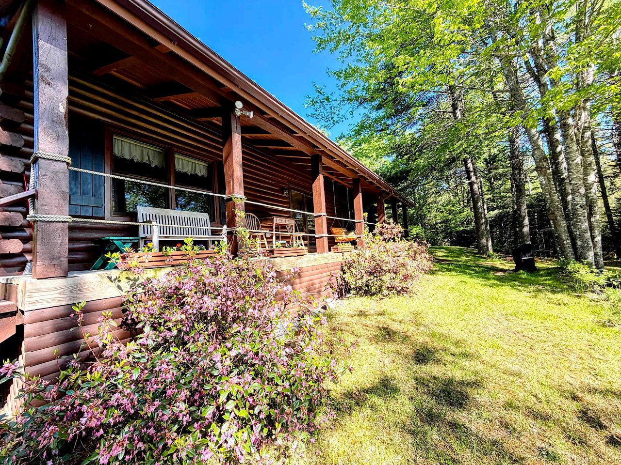 A log cabin with a porch, surrounded by a forest.