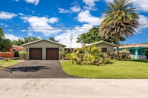 A single-story house with a garage, a well-maintained lawn, and a palm tree. - Spacious Coastal Vacation Home with Private Pool Near the Beach in Lauderdale-by-the-Sea, Florida (Lauderdale-by-the-Sea)