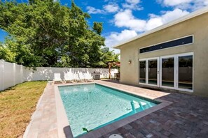 Un jardin avec une piscine, un espace patio et une clôture blanche.
