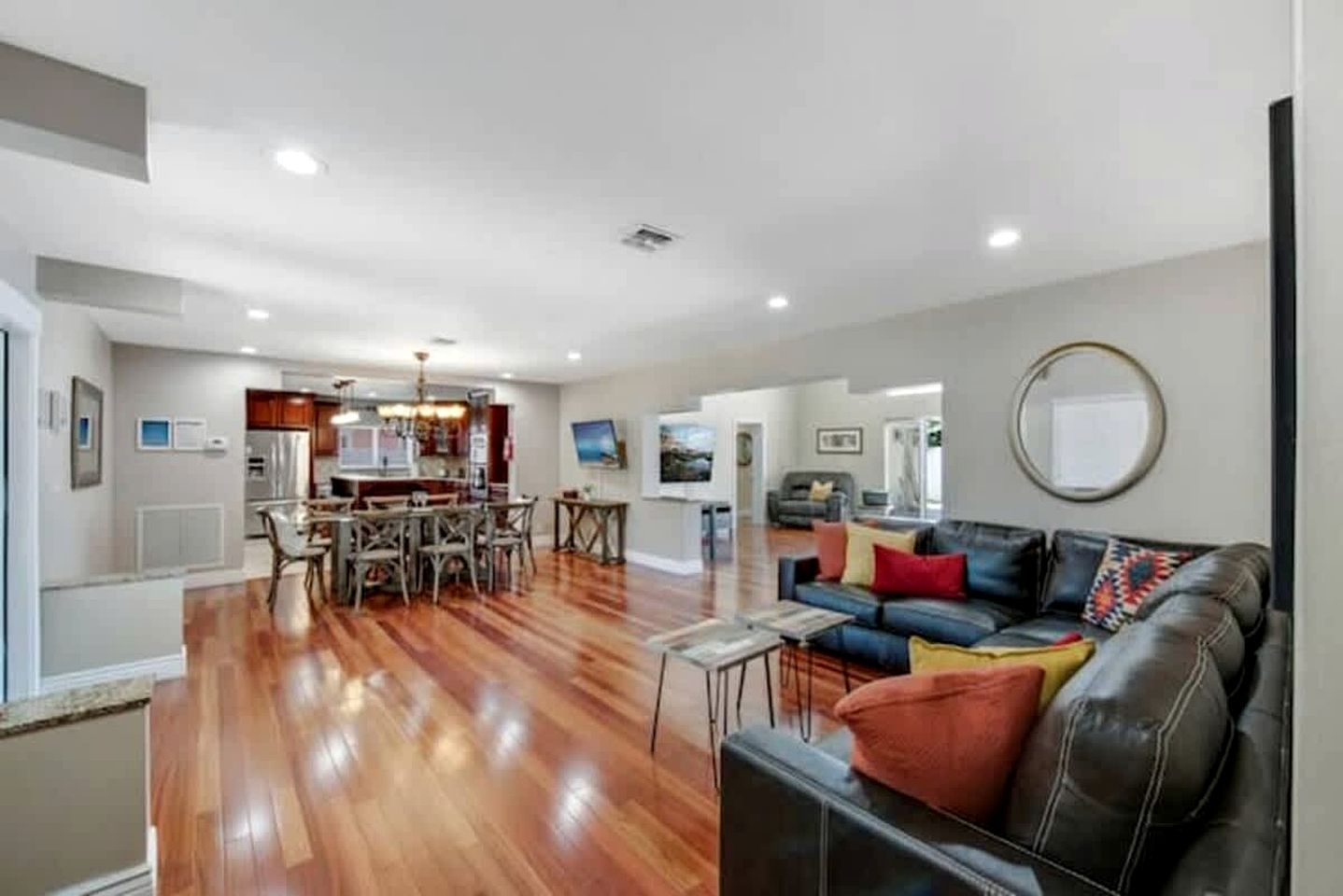 A spacious living area with a dining table, a leather sofa, and a kitchen in the background.