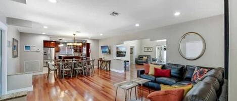A spacious living area with a dining table, a leather sofa, and a kitchen in the background.