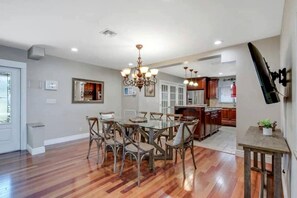 A spacious kitchen with wooden flooring, a dining area with a glass table, and a modern chandelier. - Spacious Coastal Vacation Home with Private Pool Near the Beach in Lauderdale-by-the-Sea, Florida (Lauderdale-by-the-Sea)