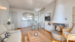 Een moderne woonkamer met een open haard, een eethoek en een keuken op de achtergrond.