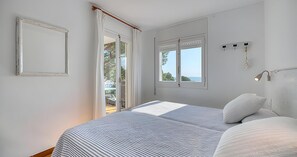Ein Schlafzimmer mit einem Bett, zwei Fenstern, einer Tür und einer Wandleuchte.