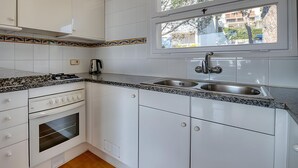 Een keuken met witte kastjes, een gasfornuis, een inbouwoven, een dubbele spoelbak en een raam met uitzicht.