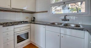 Eine Küche mit weißen Schränken, einem Gasherd, einem eingebauten Backofen, einer Spüle und einem Fenster mit Blick ins Freie.