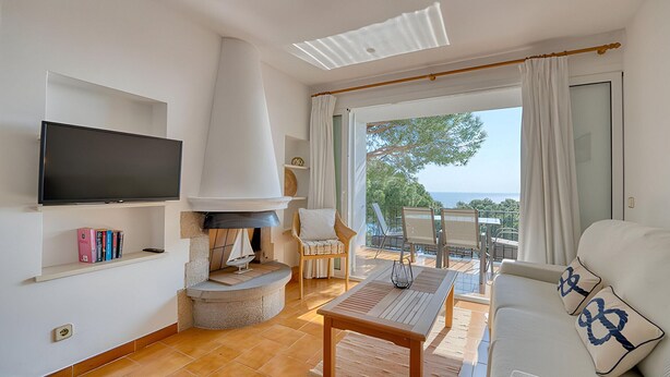 Een woonkamer met een open haard, een televisie, een bank en uitzicht op zee.