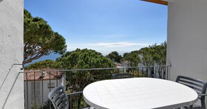 Ein Balkon mit rundem Tisch und Stühlen, mit Blick auf eine Küstenlandschaft mit Bäumen und Gebäuden.