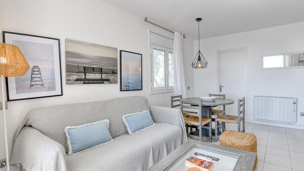 A living room with a sofa, a coffee table, a dining table with chairs, a hanging light fixture, and framed pictures on the wall. - Sea View Apartment in Calella with Parking Included (Calella de Palafrugell)