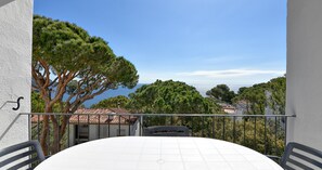 Ein Balkon mit Tisch und Stühlen, mit Blick auf eine Küstenlandschaft mit Bäumen und Gebäuden.