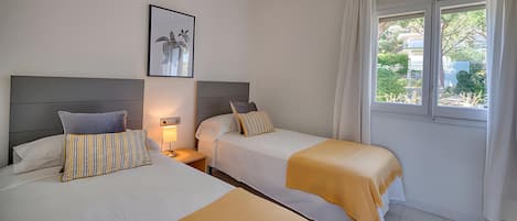 A hotel room with two beds, a nightstand, a lamp, a framed picture on the wall, and a window with curtains.