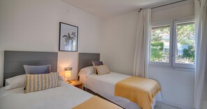 Ein Hotelzimmer mit zwei Betten, einem Nachttisch, einer Lampe, einem gerahmten Bild an der Wand und einem Fenster mit Vorhängen.