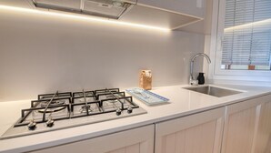 Et moderne køkken med gaskomfur, vask og et vindue med persienner.