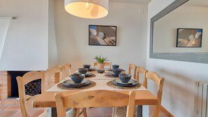 Een eetruimte met een tafel voor vier personen, houten stoelen, een potplant en kunst aan de muren.