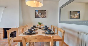 A dining area with a table set for four, wooden chairs, a potted plant, and artwork on the walls. - Charming beachfront apartment with sea views just 10 meters from the beach in Cala de Calau, Calella de Palafrugell. (Calella de Palafrugell)