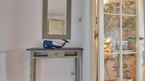 Een kamer met een witte deur, een spiegel boven een console en een blauw object op de tafel.