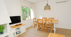 A room with a TV, wooden dining table, chairs, a hanging light fixture, and a window with a view. - Renovated accommodation with air conditioning (Calella de Palafrugell)
