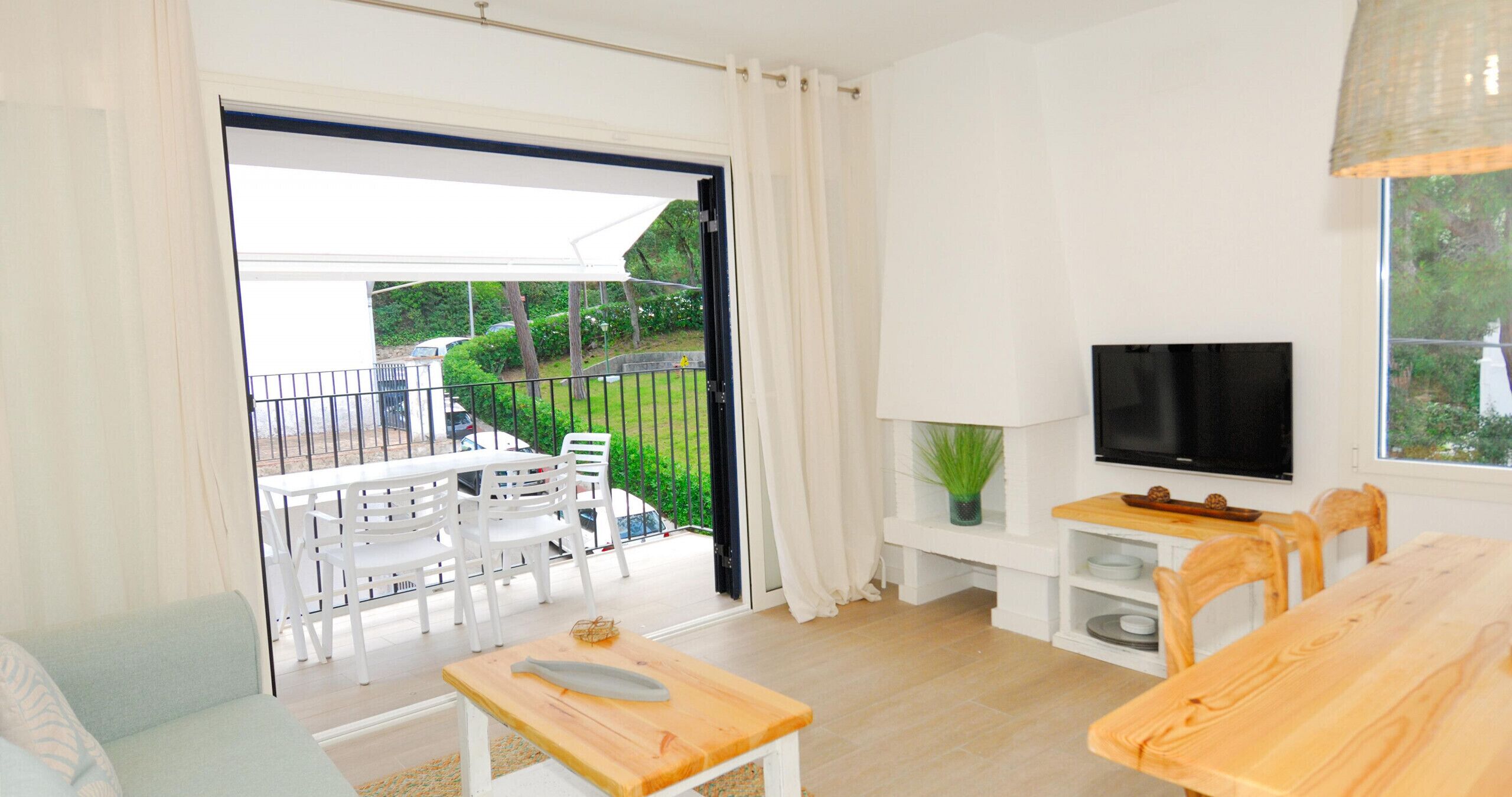 Ein modernes Wohnzimmer mit Fernseher, Holzmöbeln, einem Balkon mit Sitzgelegenheit und Blick auf Grünflächen.
