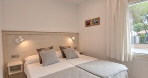 A double bed with two pillows, a bedside table, a wall-mounted light, and a window with curtains. - Renovated accommodation with air conditioning (Calella de Palafrugell)