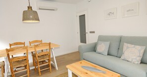 A living room with a sofa, a dining table with chairs, a hanging light fixture, and wall-mounted artwork. - Renovated accommodation with air conditioning (Calella de Palafrugell)