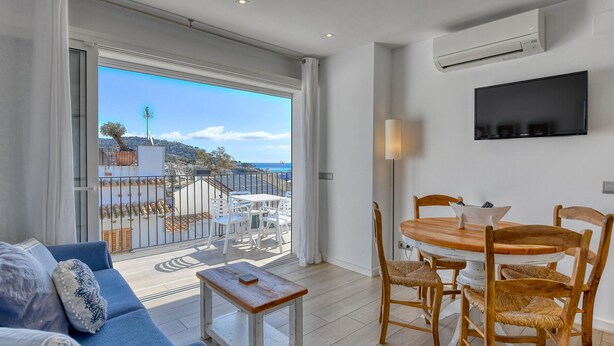 A balcony with a view of a coastal town, a dining area with a round table and chairs, and a sofa with cushions. - Studio with sea views in the center of Calella (Calella de Palafrugell)