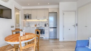 A compact kitchen with white cabinets, a stainless steel refrigerator, and a dining area with a wooden table and chairs. - Studio with sea views in the center of Calella (Calella de Palafrugell)