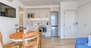 A compact kitchen with white cabinets, a stainless steel refrigerator, and a dining area with a wooden table and chairs. - Studio with sea views in the center of Calella (Calella de Palafrugell)