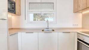A kitchen with a window, a sink, cabinets, and a stove. - Sea View Apartment in Calella, Ideal for Couples (Calella de Palafrugell)