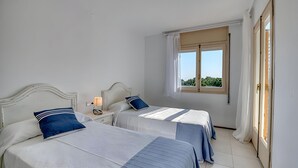 A bedroom with two beds, a nightstand, a window with curtains, and a door. - Sea View Apartment in Calella, Ideal for Couples (Calella de Palafrugell)