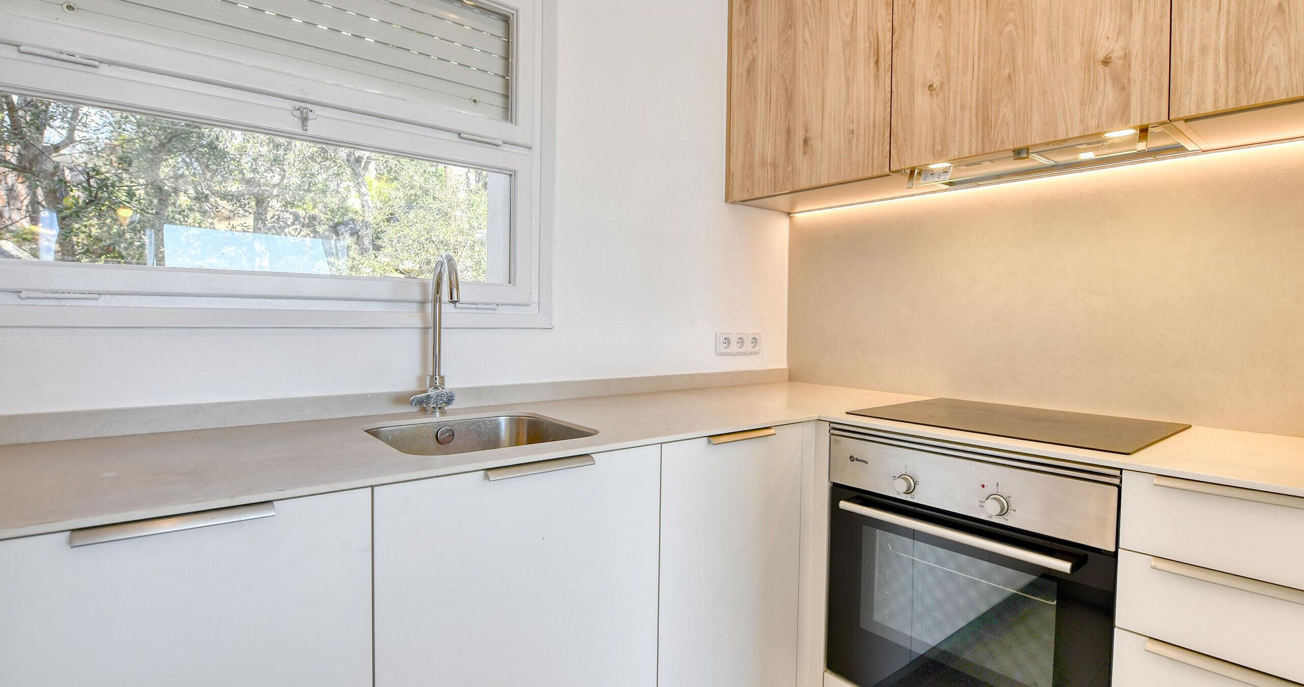 A modern kitchen with a sink, oven, and wooden cabinets.