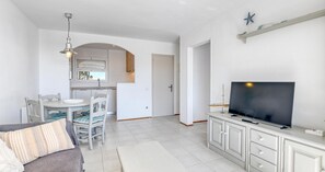 Ein modernes Wohnzimmer mit Flachbildfernseher, Essbereich mit Stühlen und einer Küche mit Fenster.
