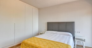 Ein Schlafzimmer mit einem Bett, einem Nachttisch, einem Kleiderschrank und einem kleinen weißen Tisch.