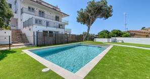 A rectangular swimming pool with a white border, surrounded by well-maintained green grass, and a multi-story building with balconies in the background. - Spectacular and spacious penthouse with communal pool in the Golfet area (Calella de Palafrugell)
