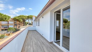 En smal balkon med trægulv, en glasdør ind til et opholdsrum, og udsigt over et boligområde med træer og bygninger.