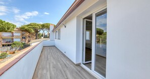 A narrow balcony with a wooden floor, a glass door leading to an interior space, and a view of a residential area with trees and buildings. - Spectacular and spacious penthouse with communal pool in the Golfet area (Calella de Palafrugell)