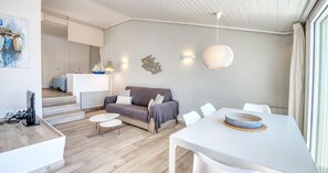 A modern living room with a sofa, two white chairs, a dining table, and a hanging light fixture. - Charming beachfront apartment with sea views just 10 meters from the beach in Cala del Calau, Calella de Palafrugell (Calella de Palafrugell)