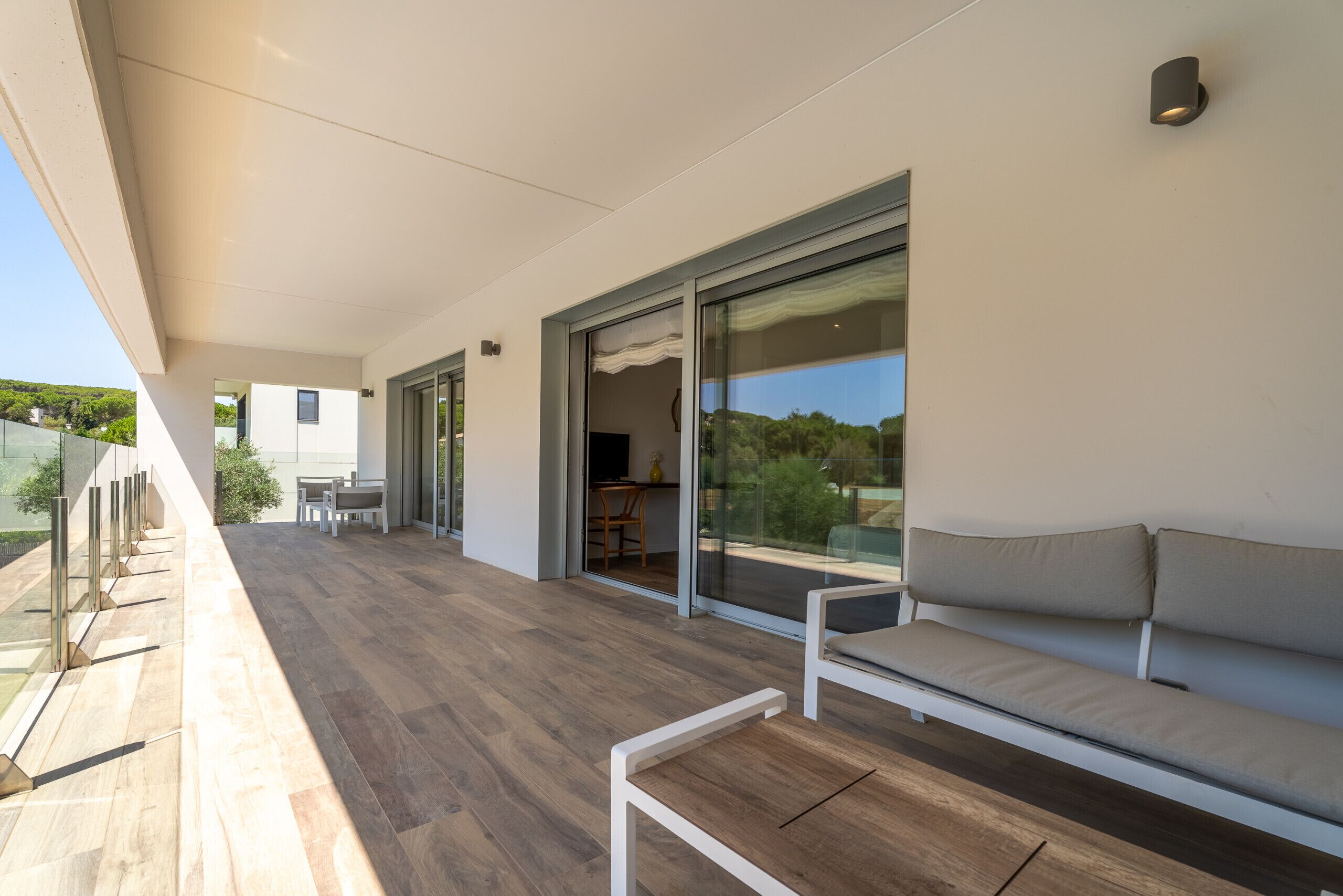 Ein moderner Balkon mit Holzboden, einer Couch und einer Essecke mit Stühlen und einem Tisch.