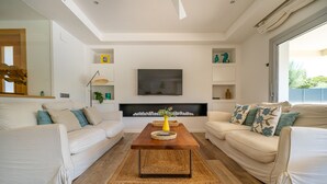 A modern living room with two sofas, a coffee table, a flat-screen TV, and decorative items on shelves. - Modern chalet with private pool (Calella de Palafrugell)