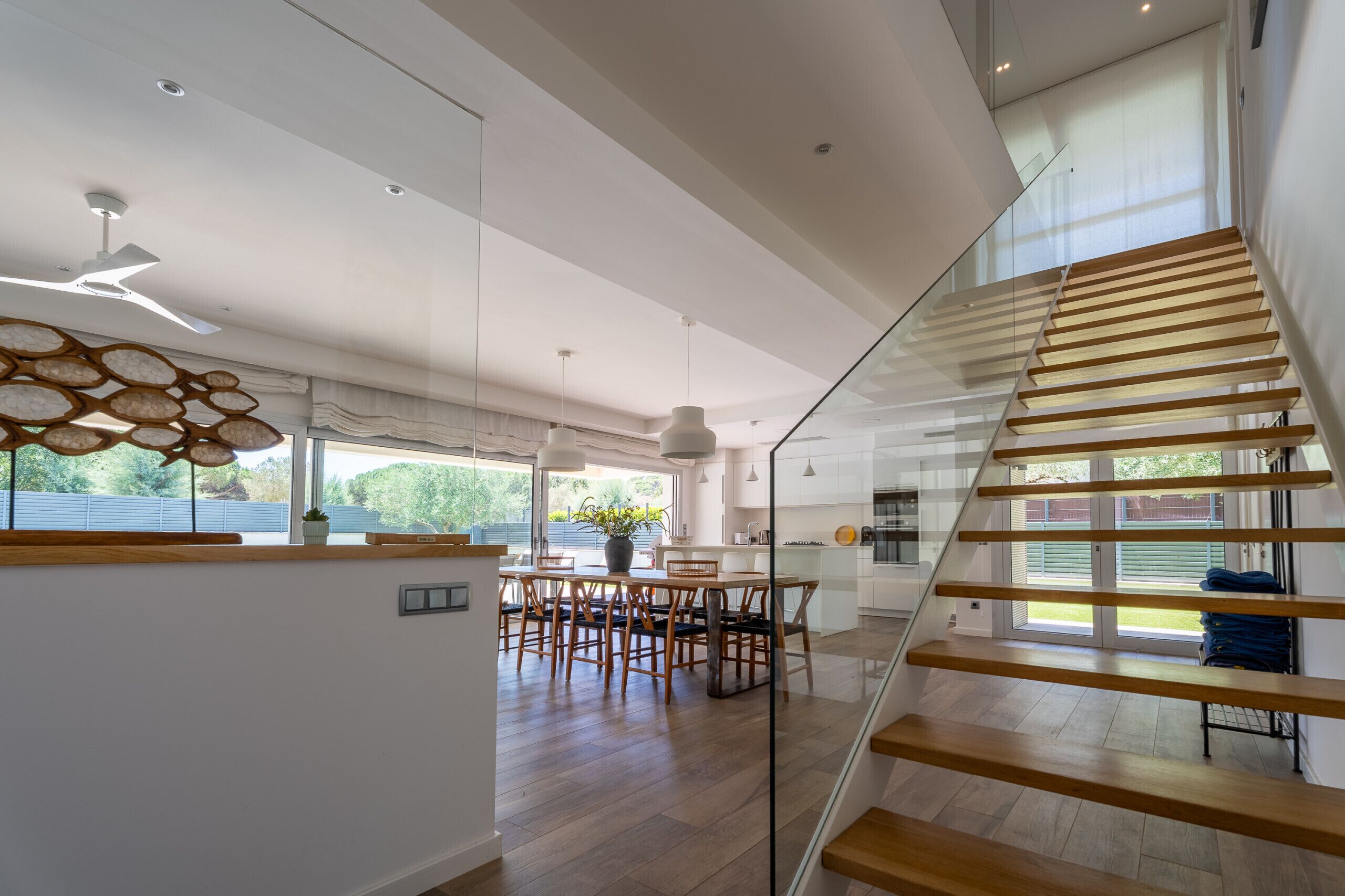 A modern interior with a glass staircase, a dining area, and a kitchen.
