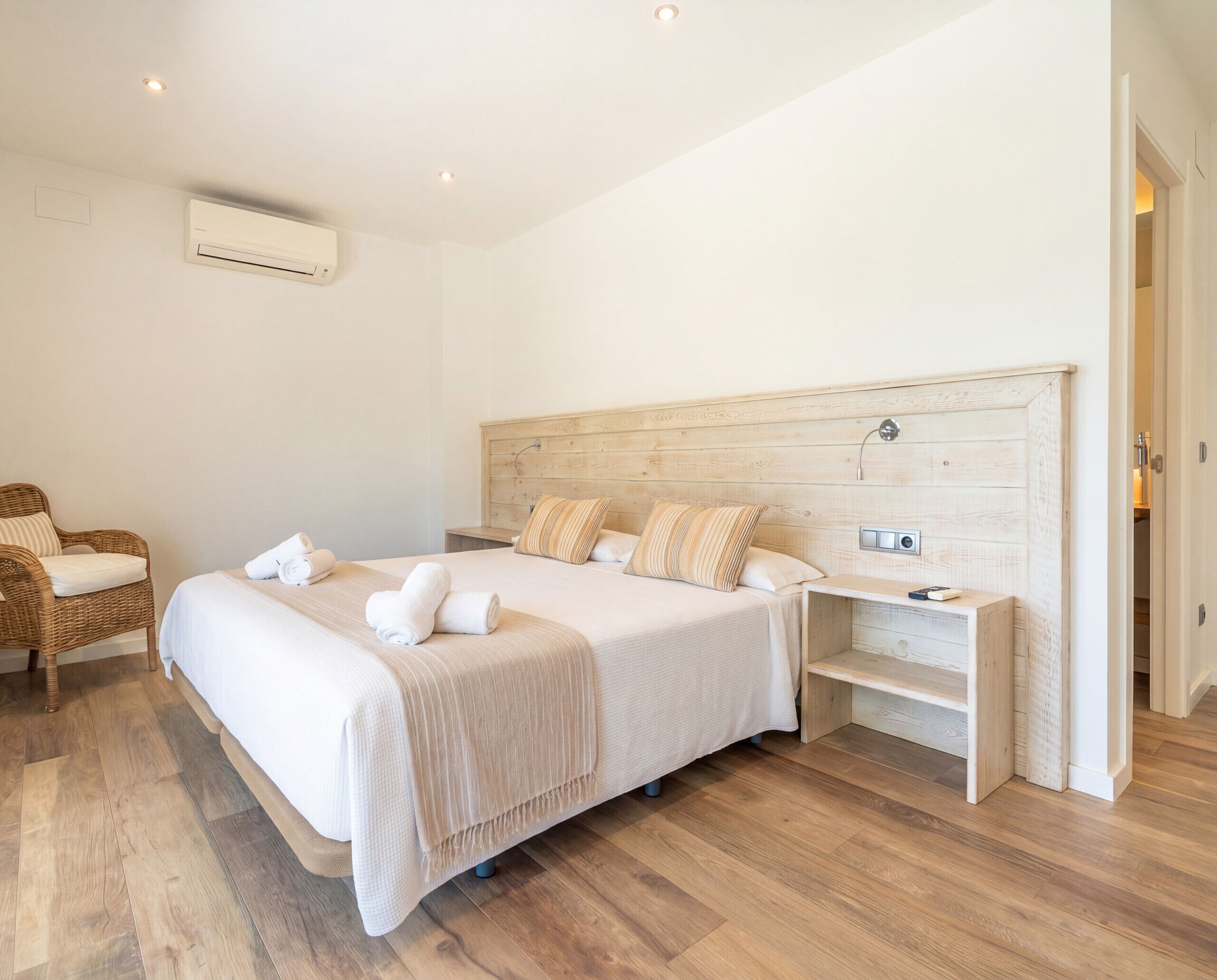 Une chambre d  ’hôtel avec un grand lit, une tête de lit en bois, une table de chevet, une chaise et un appareil de climatisation.