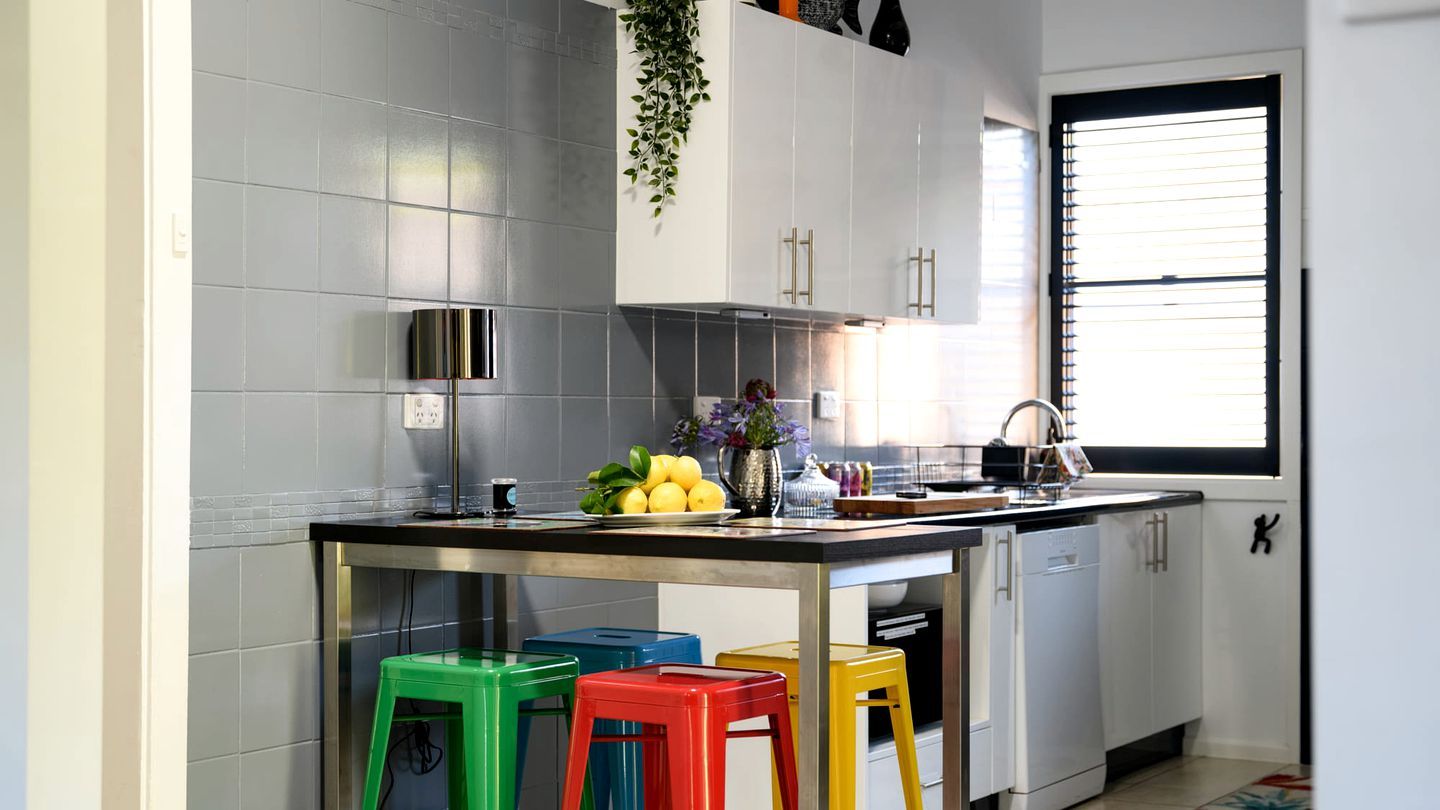 A modern kitchen with grey tiles, stainless steel appliances, and colorful stools.