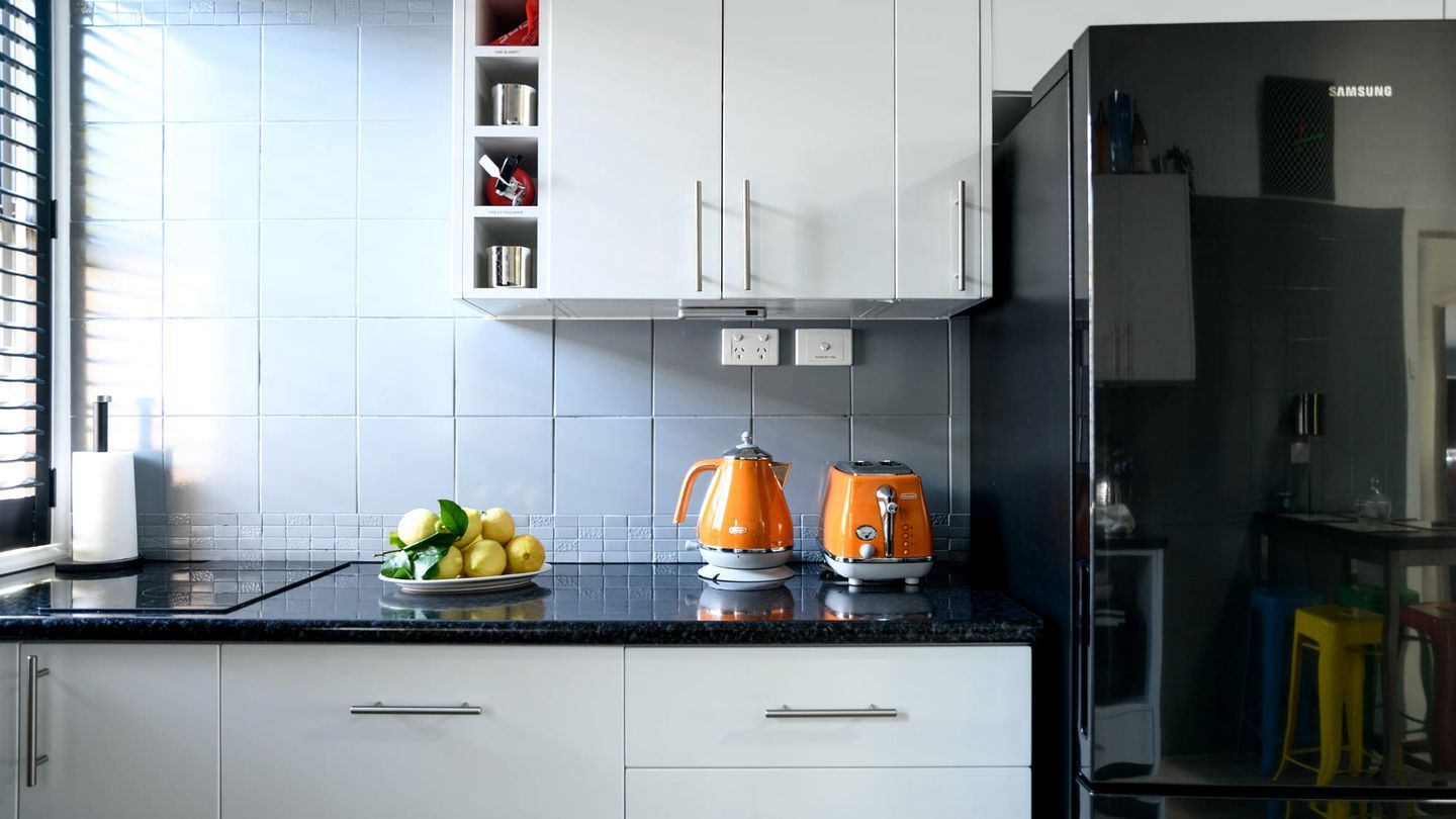 Een keuken met witte kastjes, een zwart aanrecht en een Samsung koelkast.
