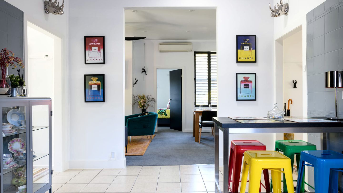 A modern kitchen with a dining area, featuring a kitchen island, colorful stools, and framed pictures on the walls.