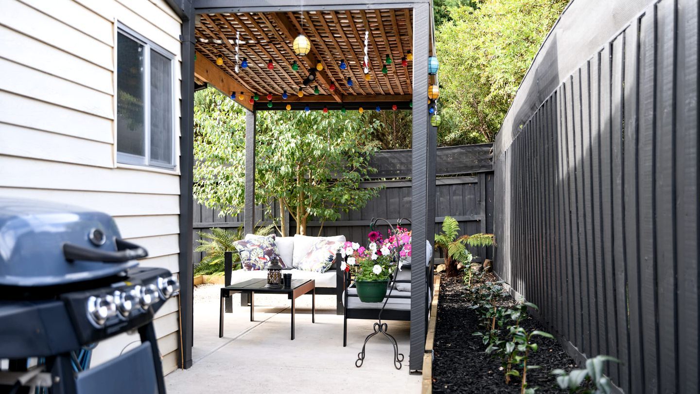 A covered patio area with a grill, a table, and a sofa.